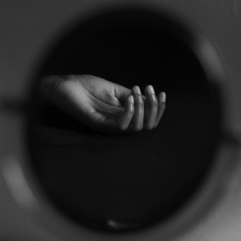 black and white photo of a hand stretching through a round, hazy opening