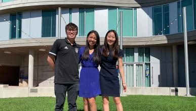 Three literary journalism students pose for a photo in front of Humanities Gateway