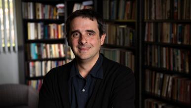 A portrait of Alex Borucki with bookshelves in the background.