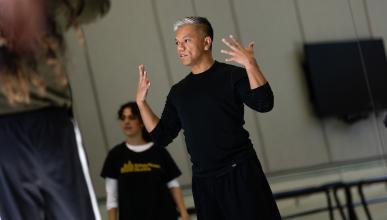 male dancer in black shirt and black pants with hands lifted to shoulders