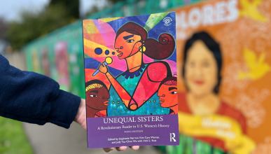 The book Unequal Sisters is held in front of a mural background