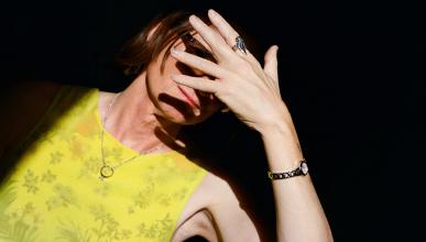 woman against black background with hand covering her face