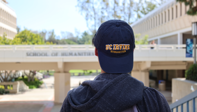A transfer student with a UC Irvine Humanities baseball cap looking at the School of Humanities bridge.