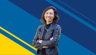 Asian American woman smiling with arms crossed standing against UCI blue and gold background