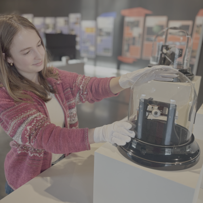 Student intern Amelia Cabrales handles a glass case with gloves while setting up an exhibition. 